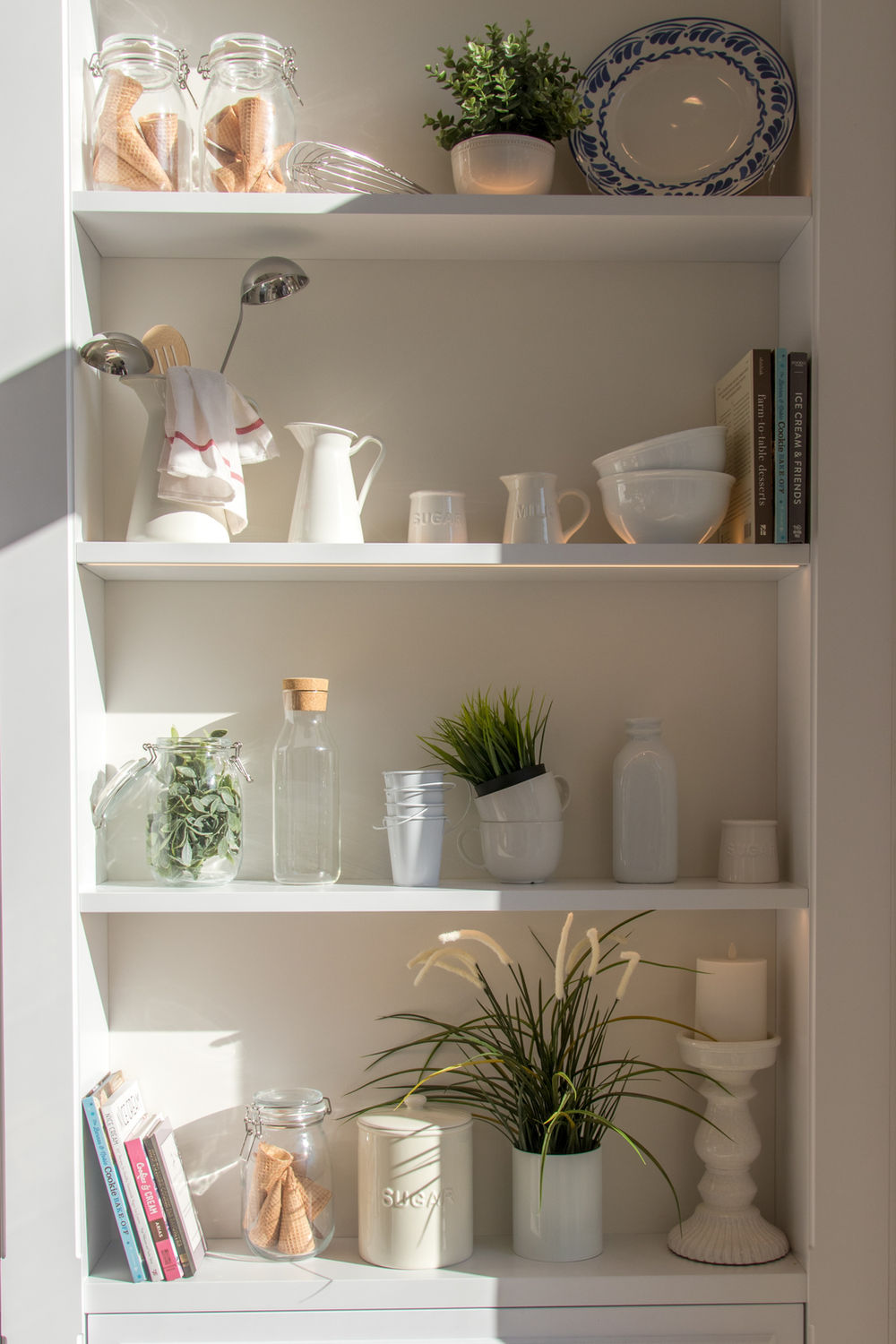 White bookshelf with four shelves holding white aesthetic pieces, clay works, and books