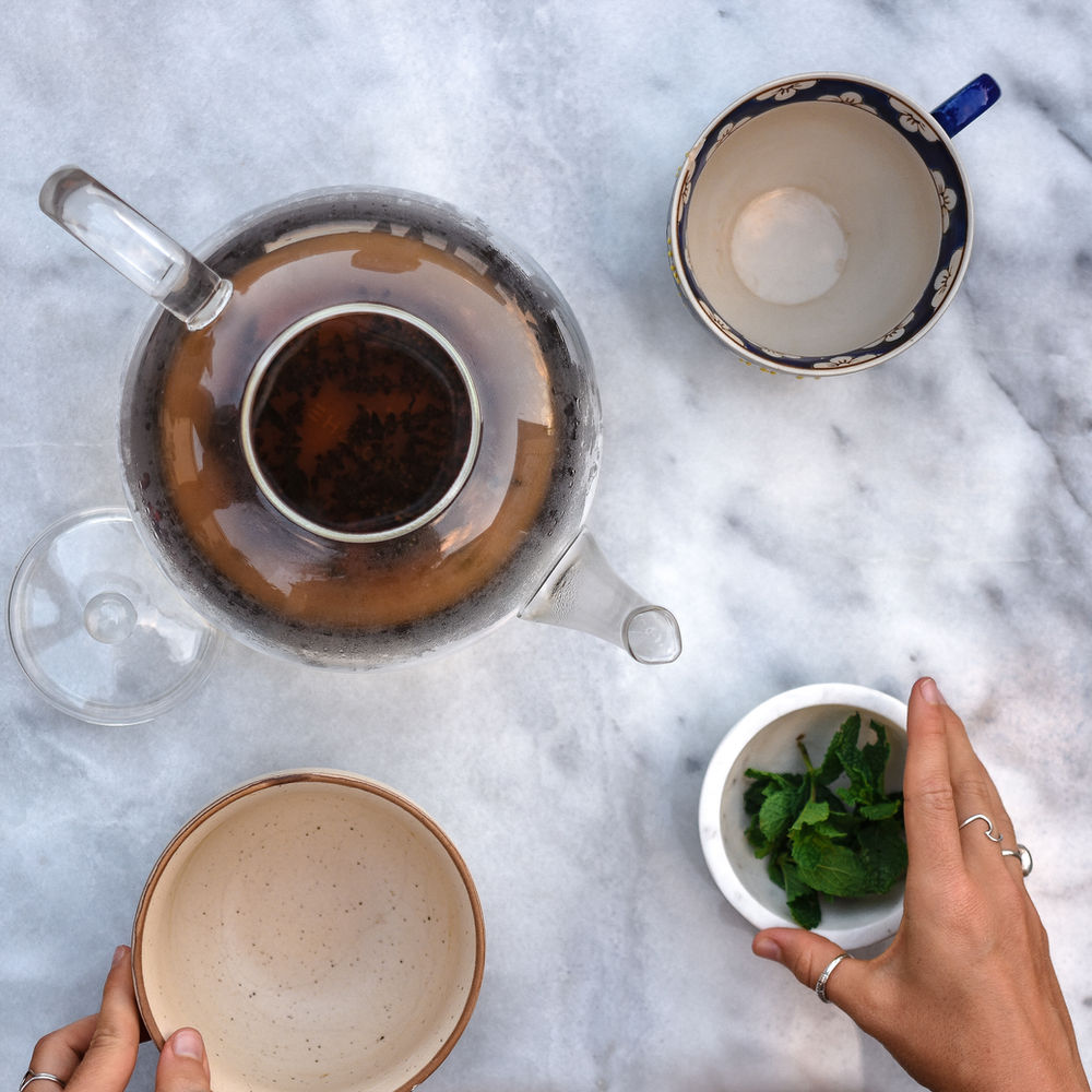 Overhead view of tea being served with a hand holding a jar of mint